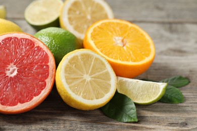 Photo of Different fresh citrus fruits and leaves on wooden table, closeup