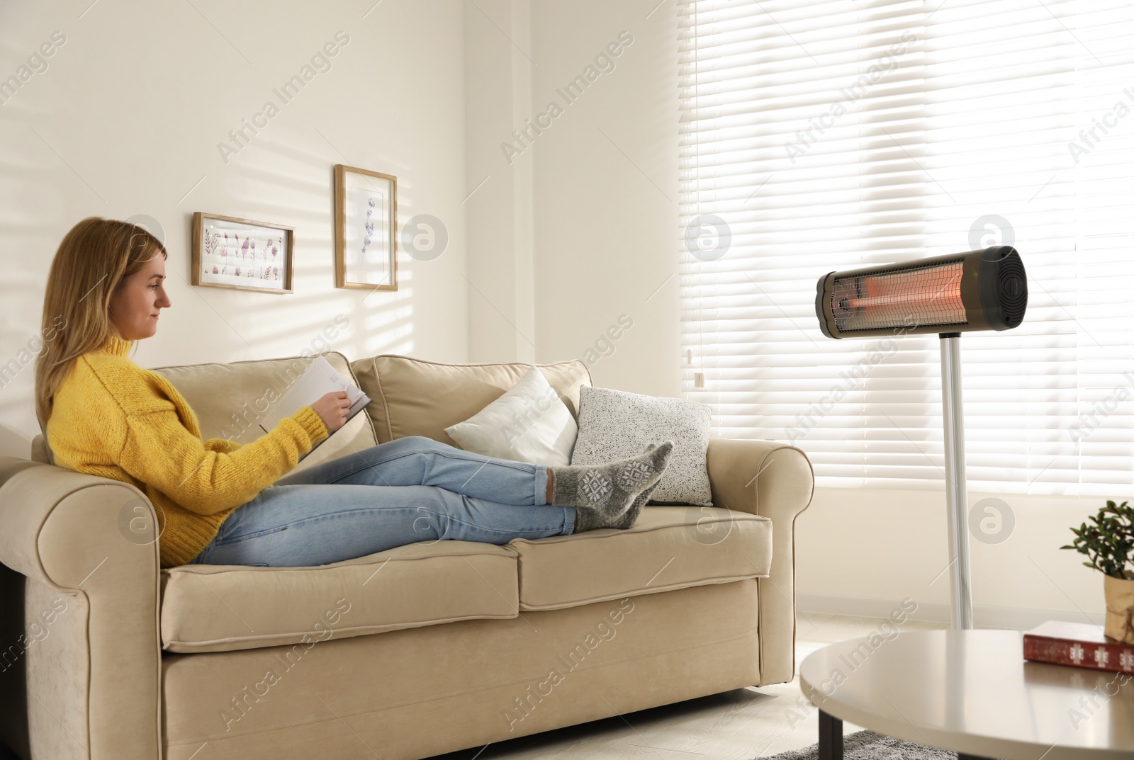 Photo of Woman reading book near electric infrared heater in living room