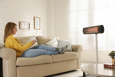 Photo of Woman reading book near electric infrared heater in living room