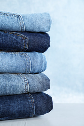 Photo of Stack of different jeans on light table against blue background