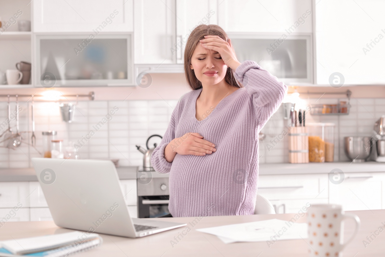 Photo of Young pregnant woman suffering from headache in home office