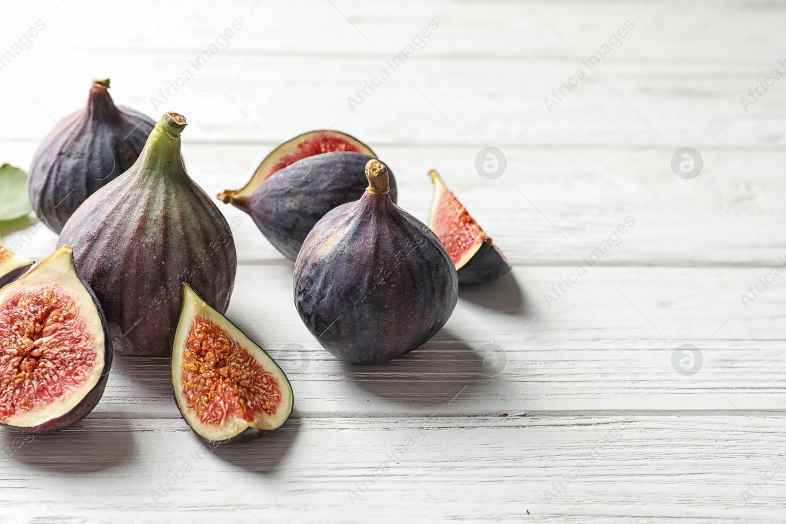 Photo of Whole and cut purple figs on wooden background. Space for text