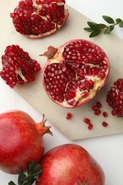 Photo of Fresh pomegranates and branches on white wooden table, flat lay