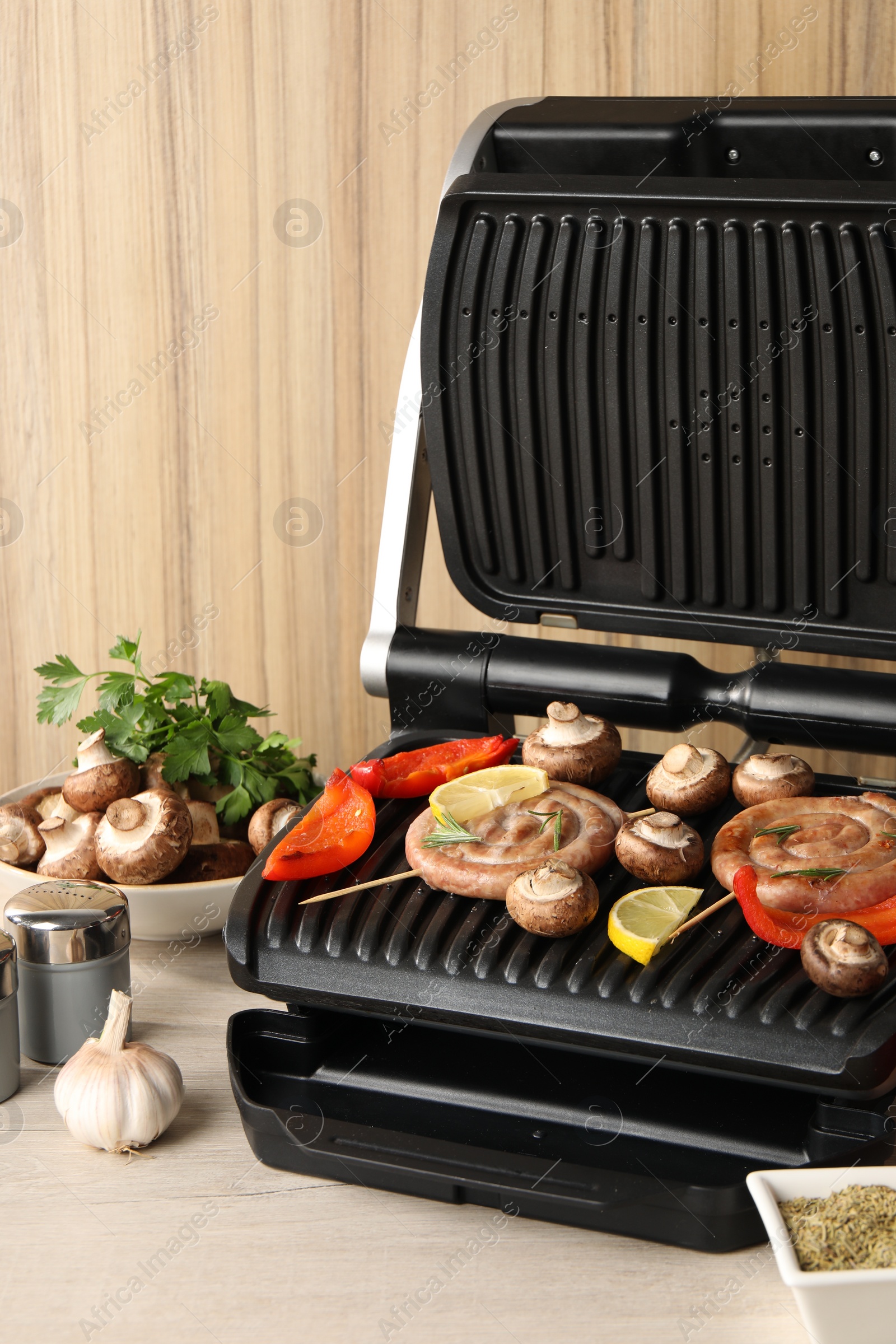 Photo of Electric grill with homemade sausages, vegetables and spices on wooden table