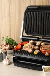 Photo of Electric grill with homemade sausages, vegetables and spices on wooden table