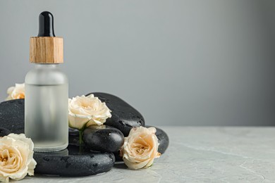 Photo of Bottle of face serum with spa stones and beautiful roses on wet table against grey background, closeup. Space for text