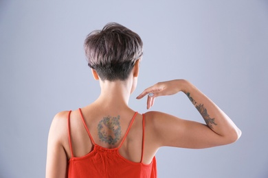 Young woman with tattoo on color background