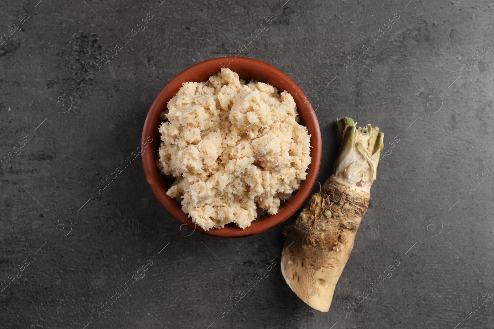 Photo of Bowl of tasty prepared horseradish and root on grey table, flat lay