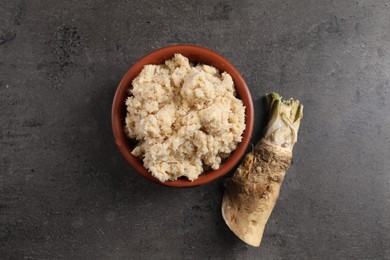 Photo of Bowl of tasty prepared horseradish and root on grey table, flat lay