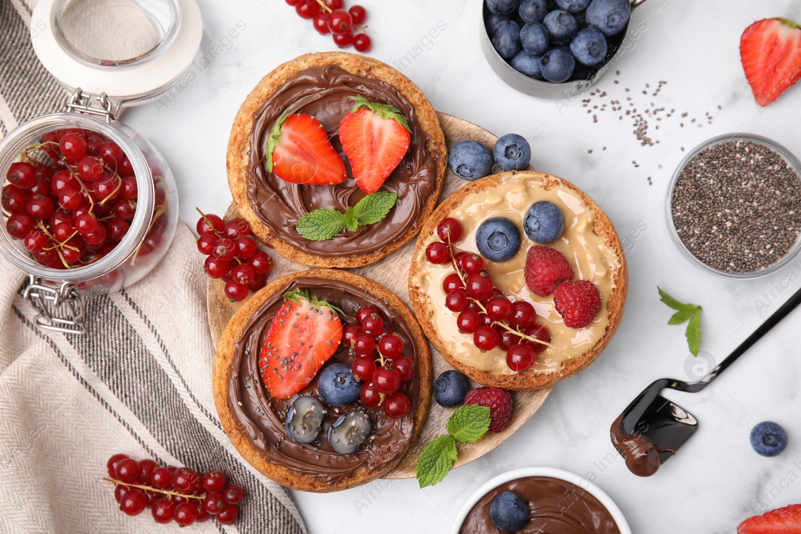 Photo of Tasty organic rusks with different toppings and ingredients on white marble table, flat lay