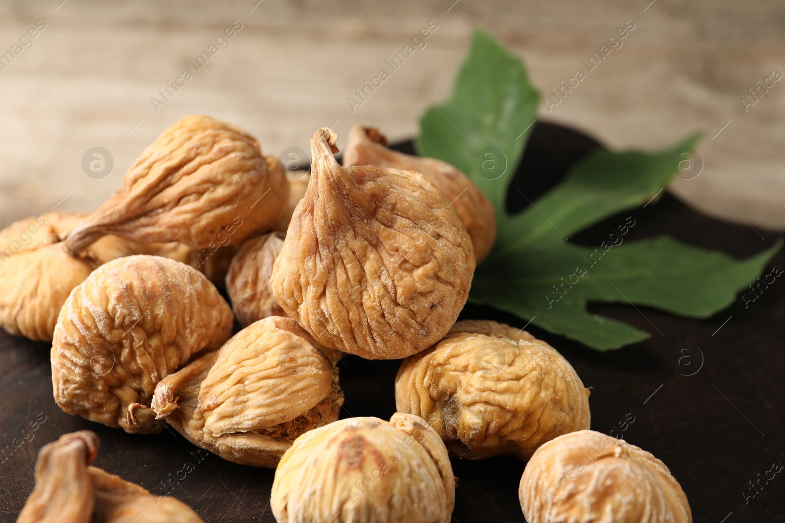 Photo of Tasty dried figs and green leaf on wooden board, closeup