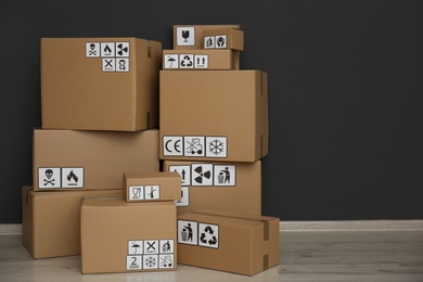 Photo of Cardboard boxes with different packaging symbols on floor near black wall. Parcel delivery