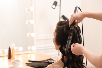 Hair styling. Hairdresser curling woman's hair in salon, closeup. Space for text