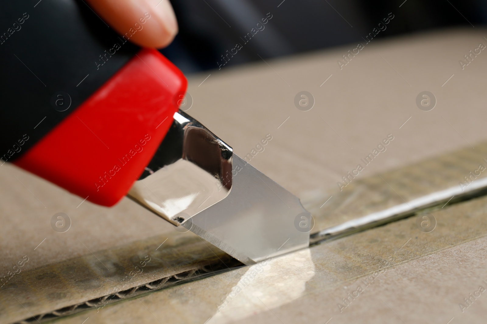 Photo of Man using utility knife to open parcel, closeup