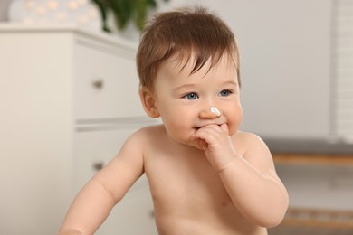 Cute little baby with moisturizing cream on face indoors