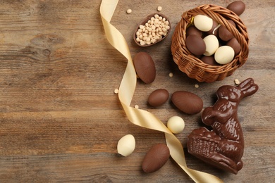 Photo of Chocolate Easter bunny and eggs on wooden table, flat lay. Space for text