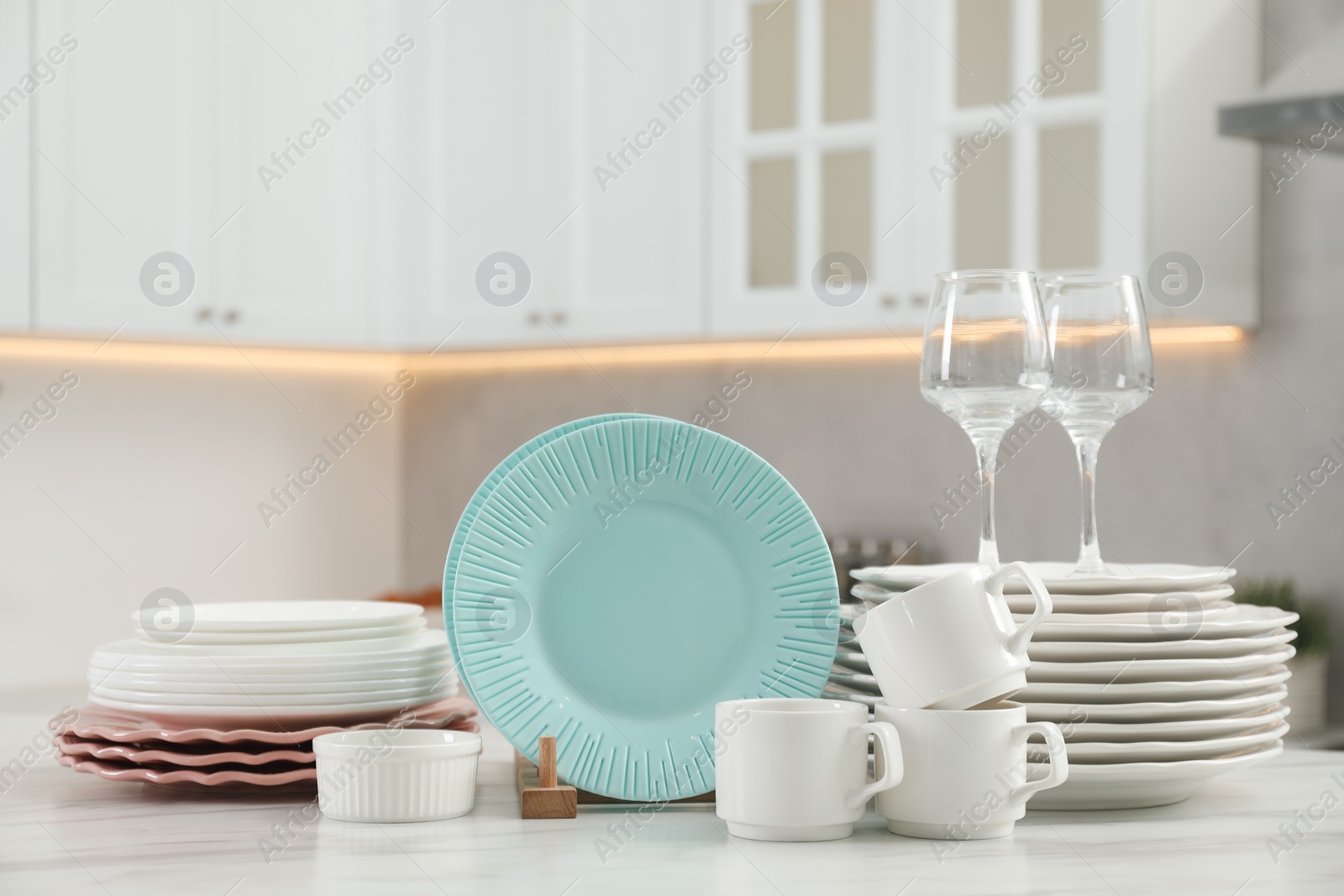 Photo of Clean plates, cups, glasses and bowl on white marble table in kitchen