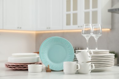 Clean plates, cups, glasses and bowl on white marble table in kitchen