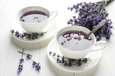 Photo of Fresh delicious tea with lavender and beautiful flowers on white wooden table