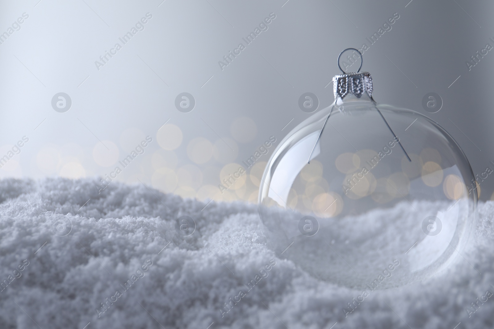 Photo of Transparent Christmas ball on snow against blurred fairy lights, space for text