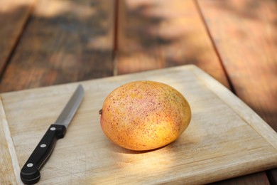 Photo of Board with tasty mango and knife on wooden table outdoors