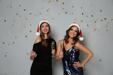 Photo of Happy women in Santa hats with champagne and confetti on grey background. Christmas party