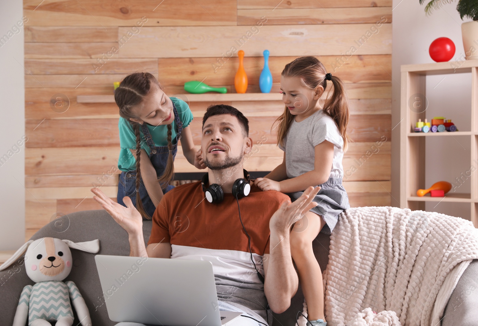 Photo of Children disturbing stressed man in living room. Working from home during quarantine