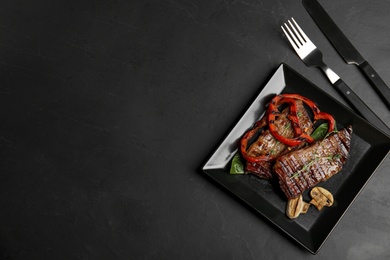 Photo of Grilled meat served with garnish on black table, flat lay. Space for text