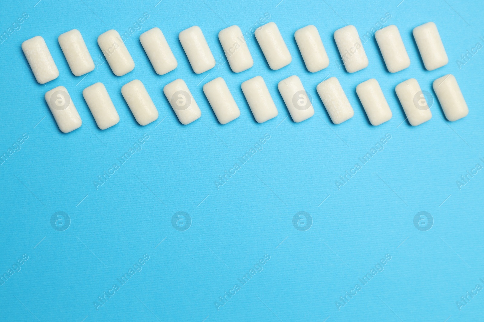 Photo of White bubble gums on blue background, flat lay. Space for text