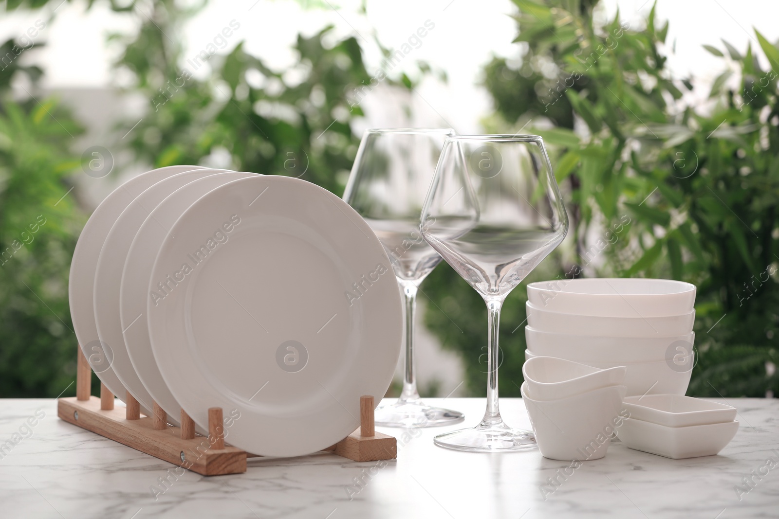 Photo of Setclean dishware and wineglasses on white table against blurred background