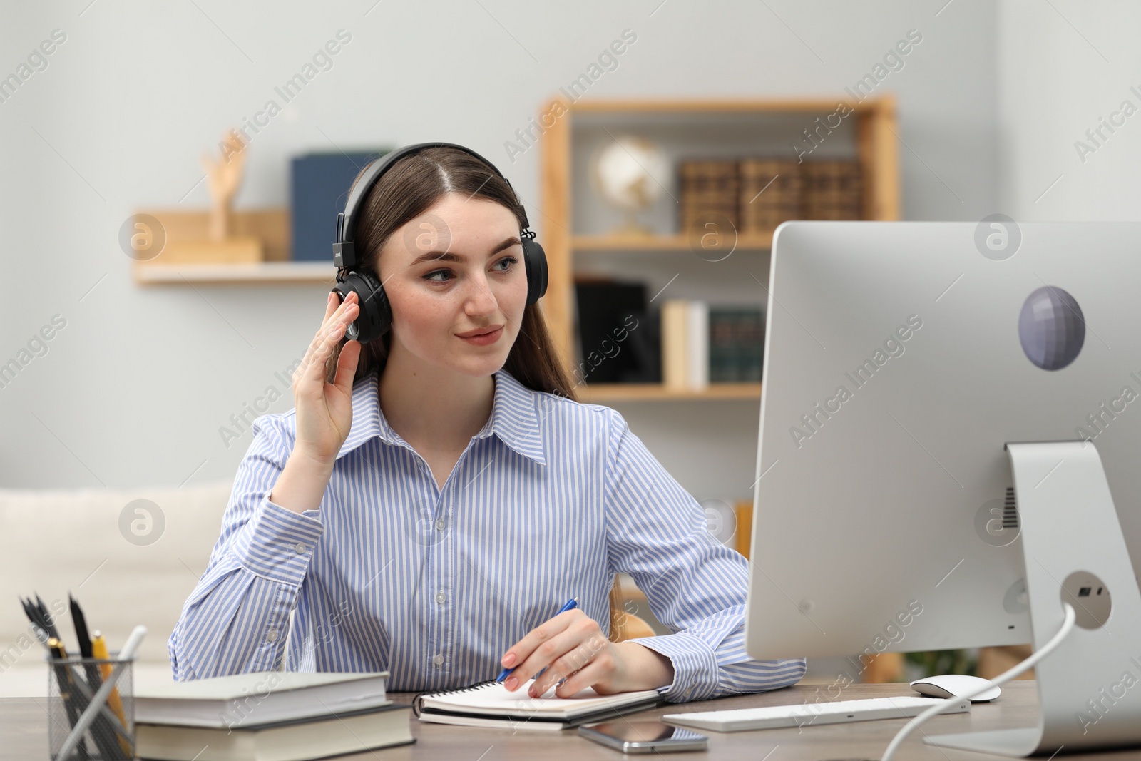 Photo of E-learning. Young woman taking notes during online lesson at table indoors