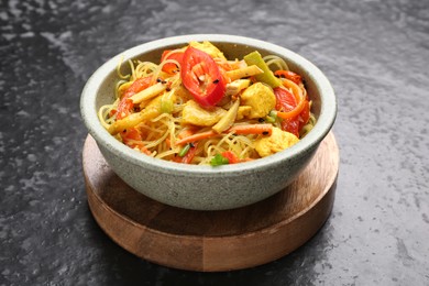 Photo of Stir-fry. Tasty noodles with vegetables and meat in bowl on dark textured table