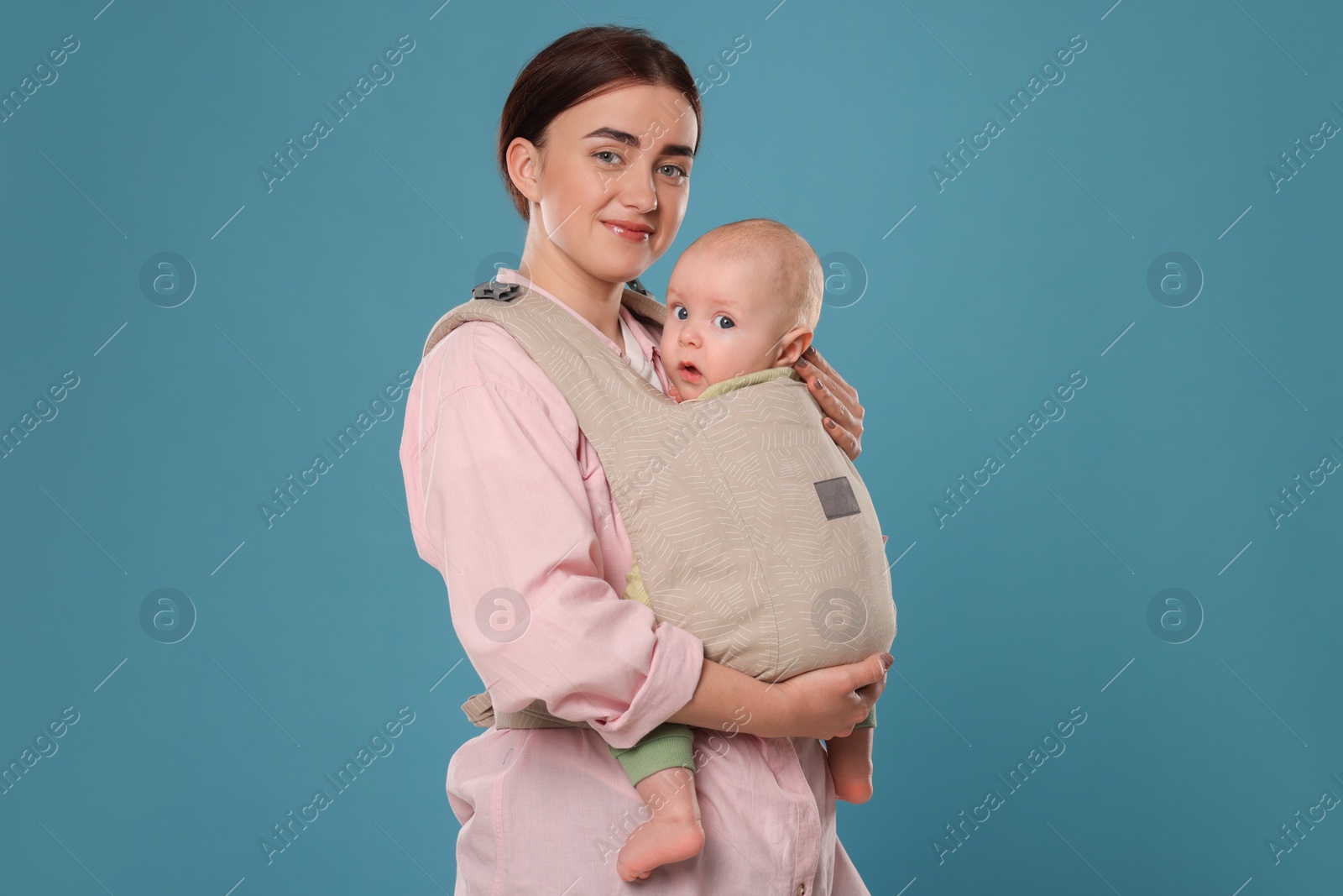 Photo of Mother holding her child in sling (baby carrier) on light blue background