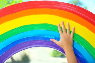 Photo of Child touching picture of rainbow on window, closeup. Stay at home concept