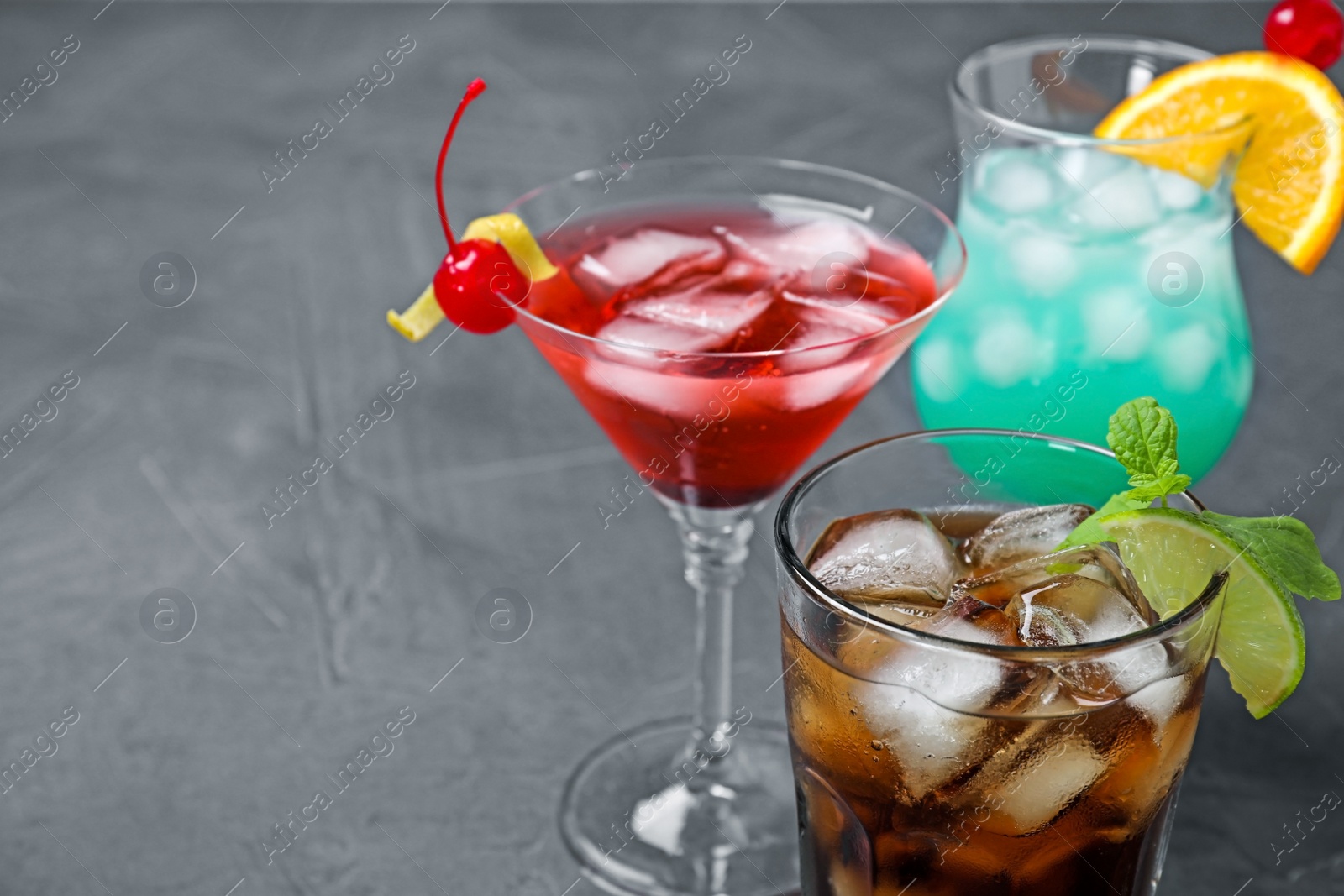 Photo of Tasty refreshing cocktails in glasses on grey stone table, closeup view. Space for text