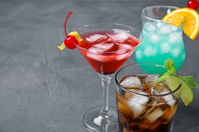 Photo of Tasty refreshing cocktails in glasses on grey stone table, closeup view. Space for text