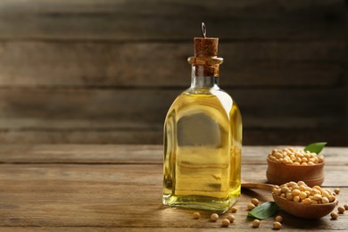 Photo of Glass bottle of oil and soybeans on wooden table. Space for text