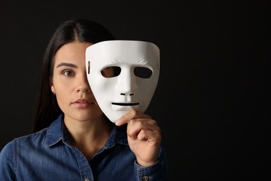 Photo of Multiple personality concept. Woman with mask on black background, space for text