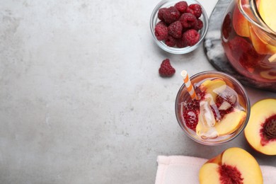 Photo of Flat lay composition of delicious peach lemonade with soda water and raspberries on grey table, space for text. Fresh summer cocktail