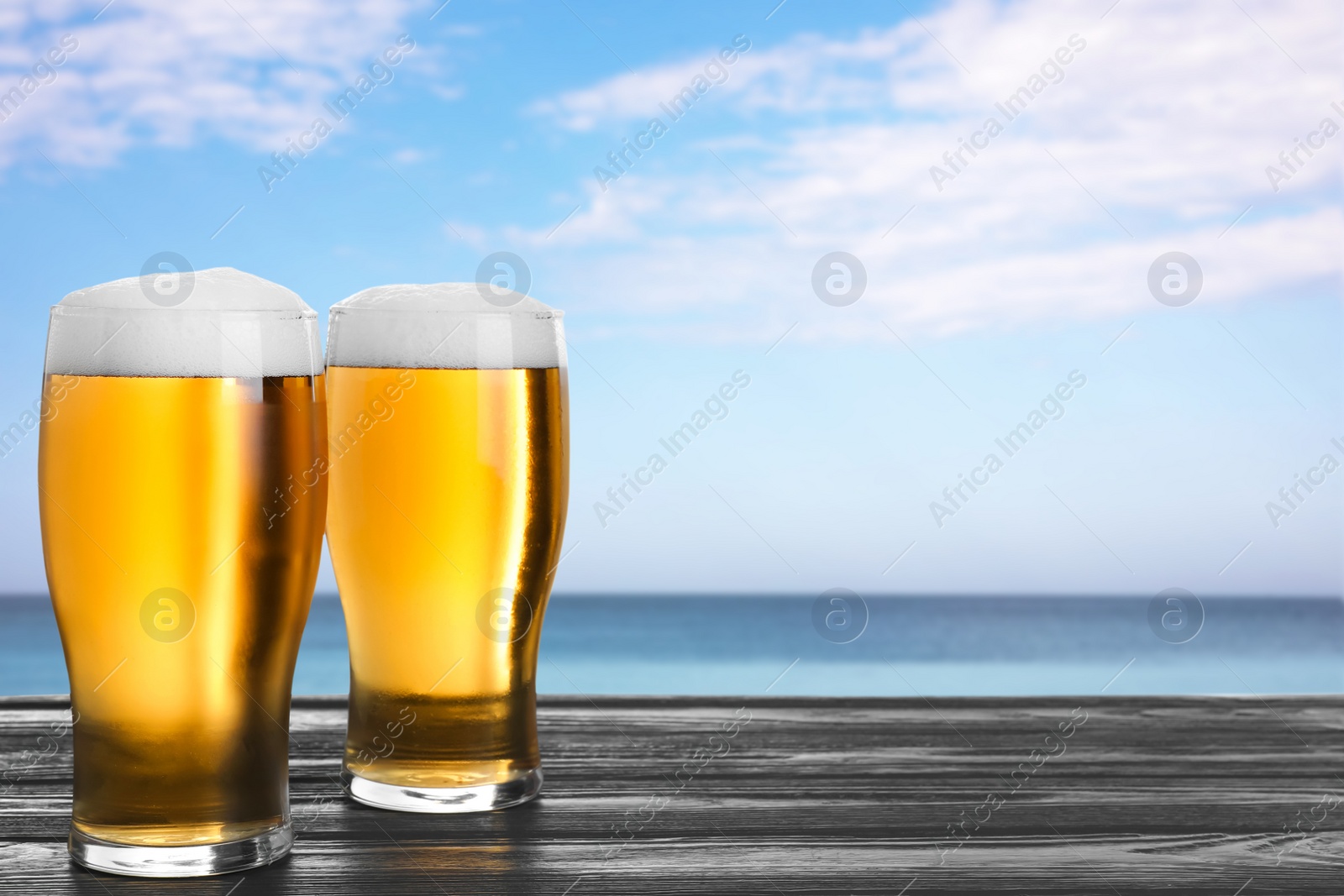 Image of Cold beer on wooden desk against blurred sea. Space for text