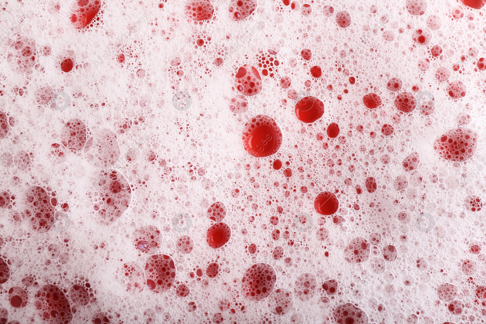 Photo of White foam with bubbles on red background, top view