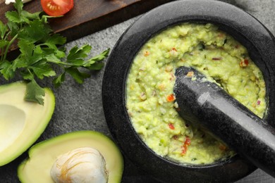 Photo of Mortar with delicious guacamole and ingredients on grey table, flat lay