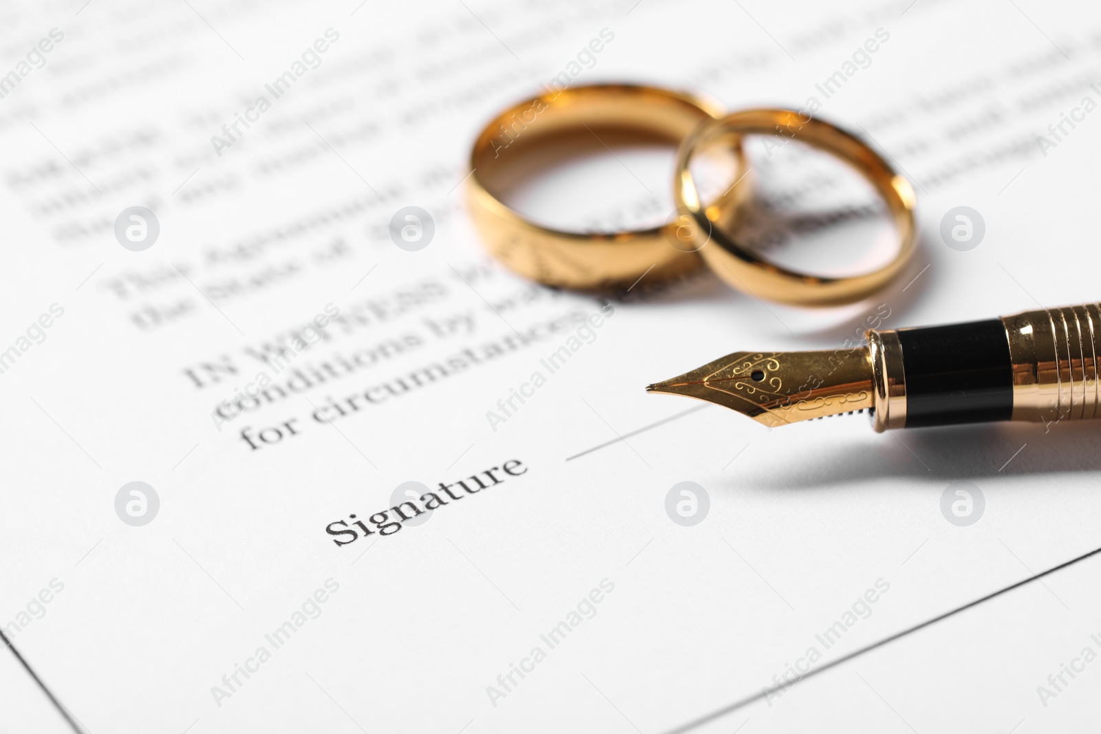 Photo of Marriage contract, gold rings and pen on table, closeup