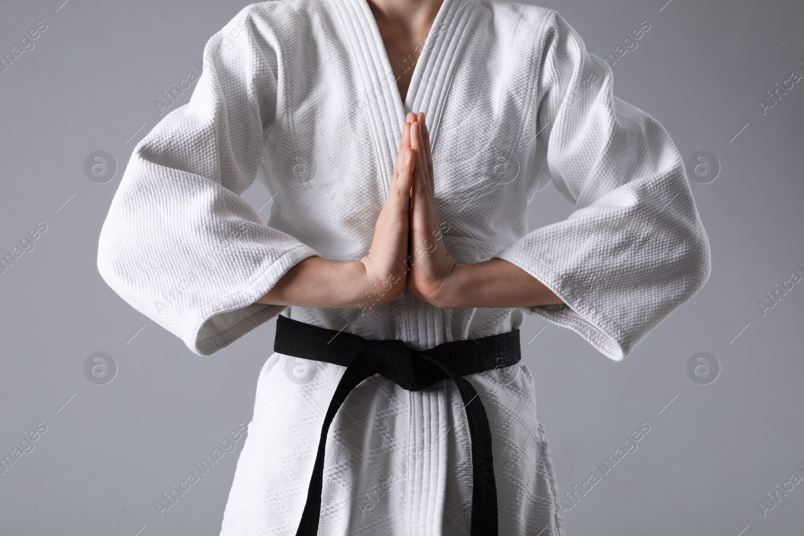 Photo of Martial arts master in keikogi with black belt on grey background, closeup