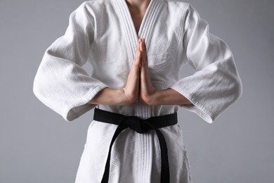 Photo of Martial arts master in keikogi with black belt on grey background, closeup