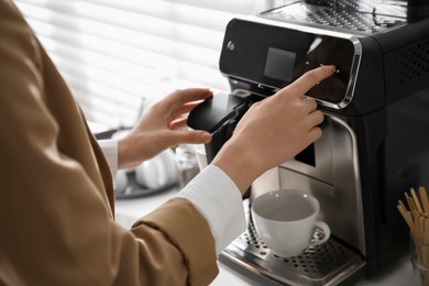 Photo of Young woman preparing fresh aromatic coffee with modern machine in office, closeup