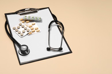 Photo of Stethoscope, pills and clipboard on beige background. Space for text