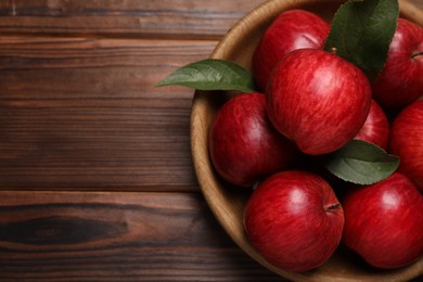 Photo of Ripe red apples and green leaves in bowl on wooden table, top view. Space for text