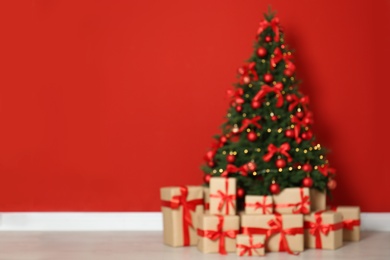 Photo of Blurred view of decorated Christmas tree and gift boxes near red wall. Space for text