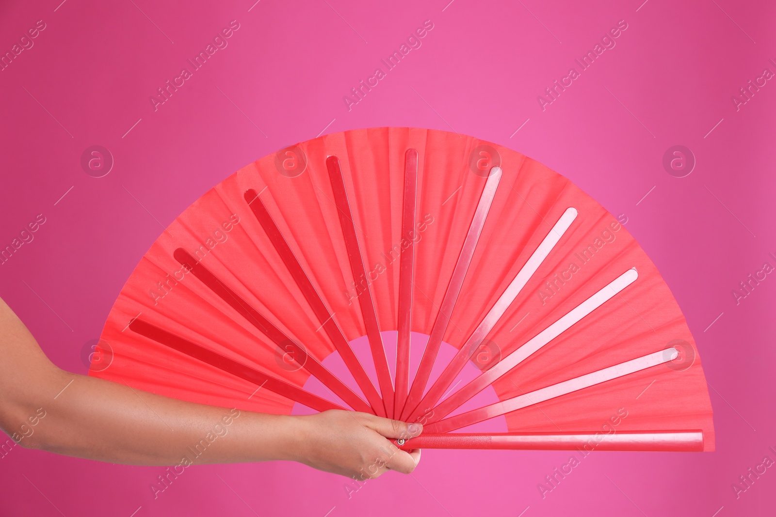 Photo of Woman holding red hand fan on pink background, closeup
